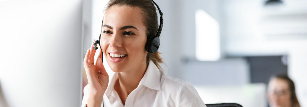 Emotional business woman in office callcenter working with computer wearing headphones.